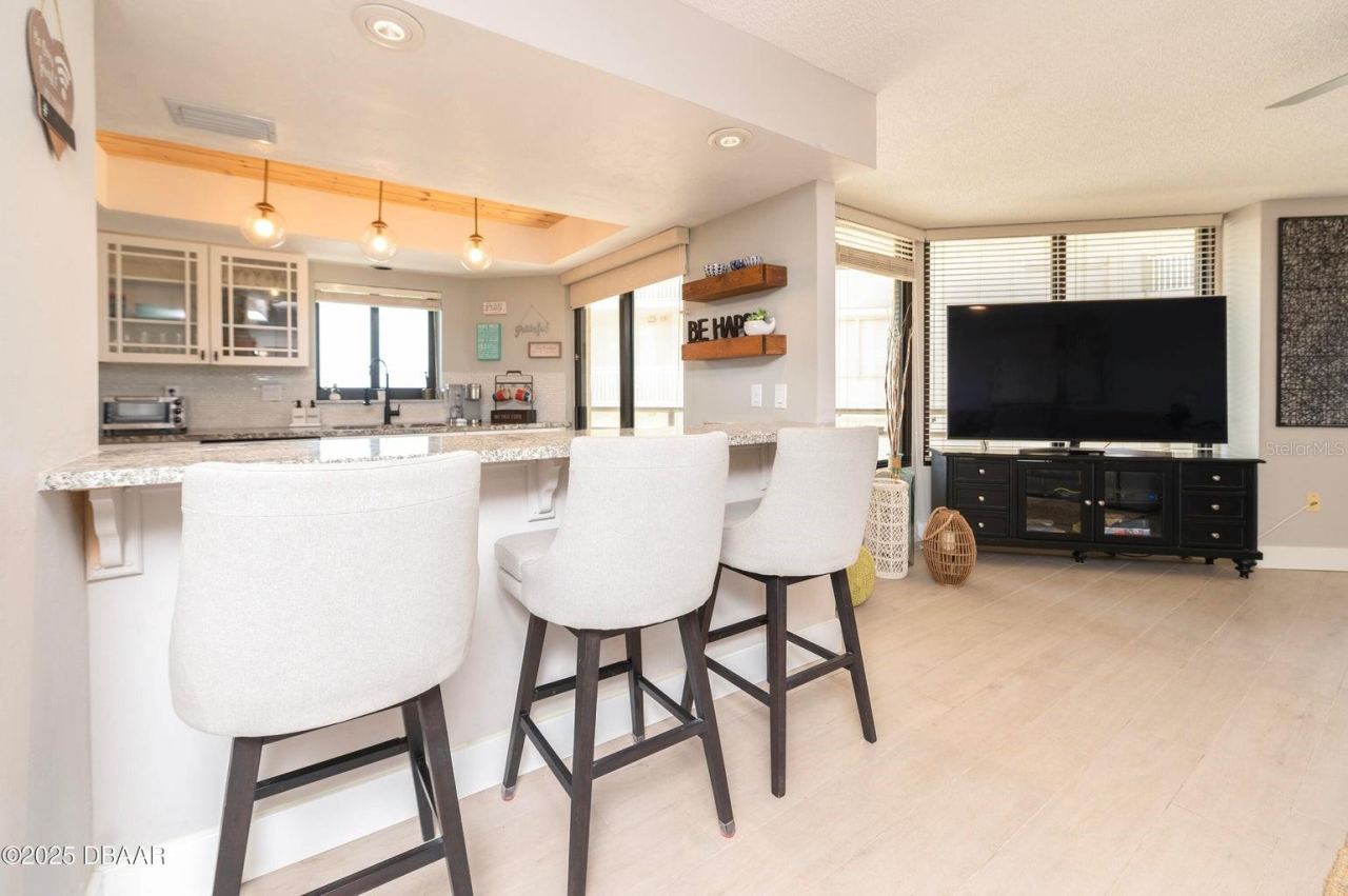 Photo 12 of 20: The kitchen flows effortlessly into the living area, with a spacious breakfast bar, contemporary lighting, and large windows creating a comfortable setting for everyday living and entertaining.
