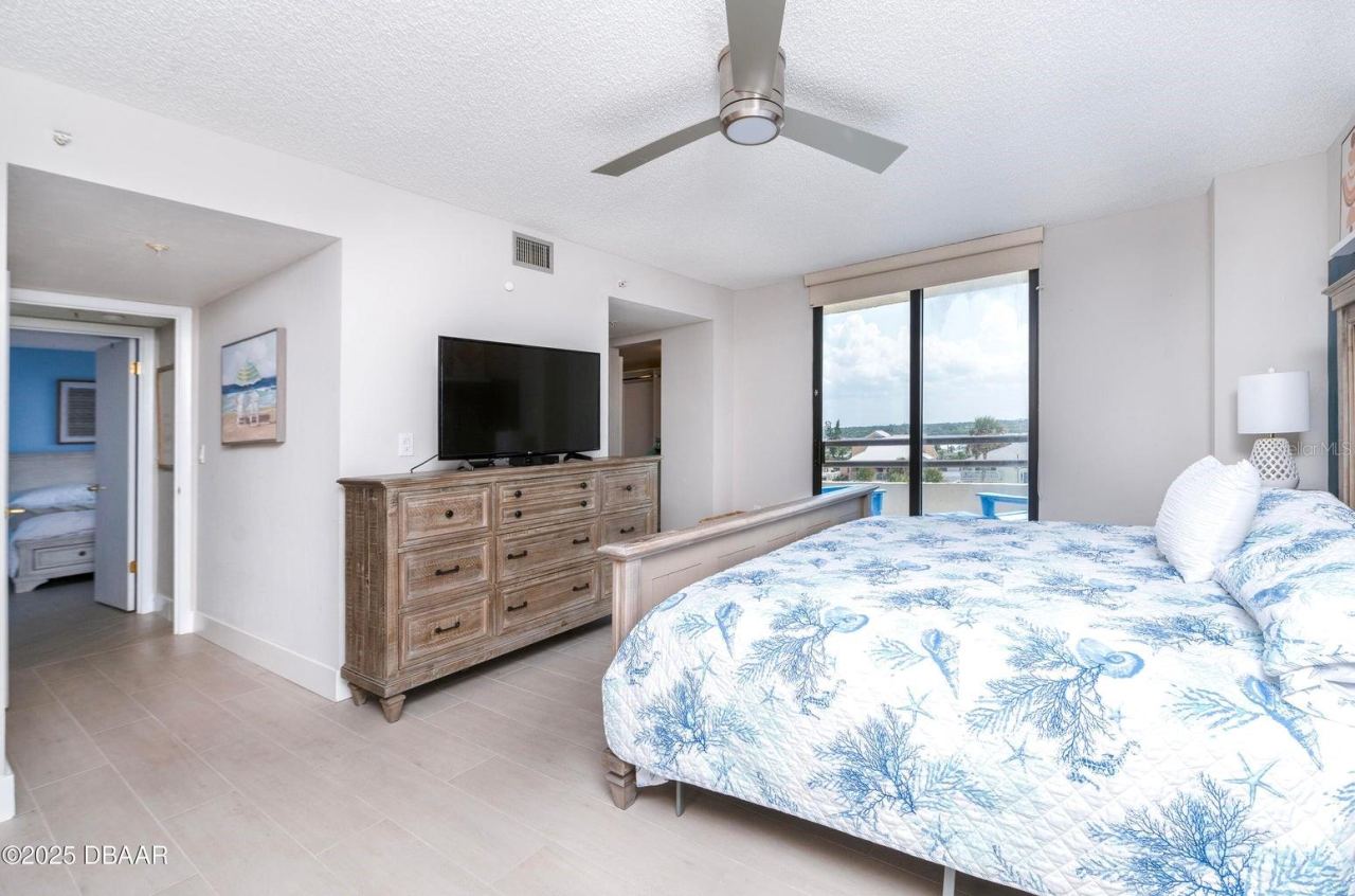 Photo 19 of 20: Another view of the generously sized primary bedroom showcases abundant natural light, neutral finishes, and direct balcony access, creating a comfortable coastal retreat.