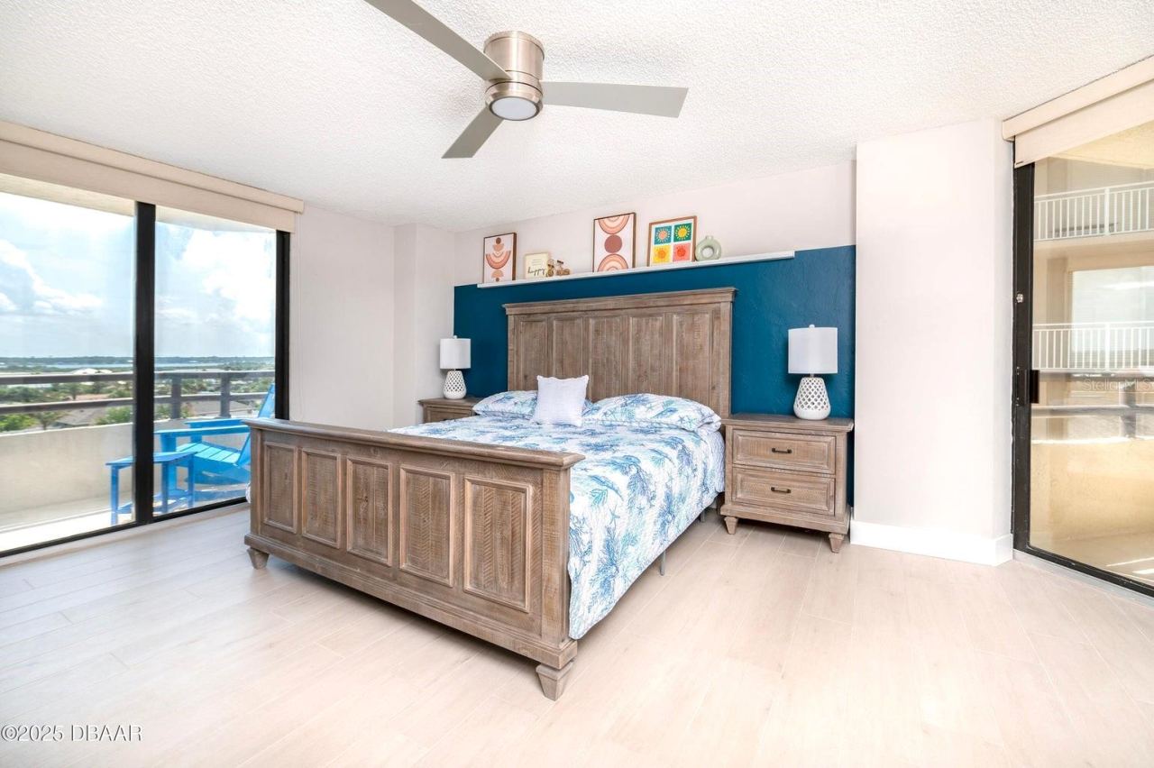 Photo 18 of 20: This spacious primary suite features a striking blue accent wall, contemporary ceiling fan, and sliding glass doors opening to a private balcony with scenic inland views.