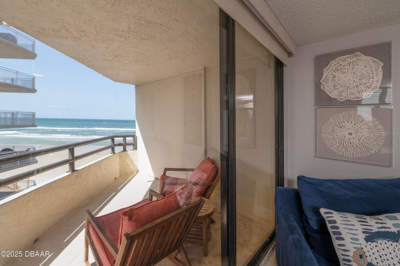 Photo 16 of 20: Floor-to-ceiling sliding glass doors connect the living room to the covered oceanfront balcony, offering an effortless transition between indoor comfort and outdoor relaxation.