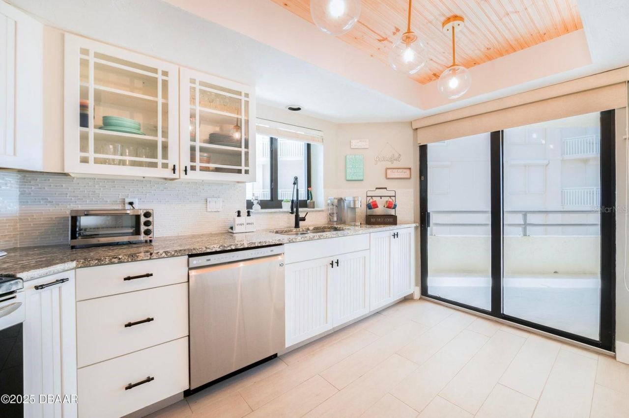 Photo 9 of 20: Beautifully appointed kitchen featuring white cabinetry, granite countertops, a stylish tile backsplash, and glass-front upper cabinets. A wood-accented tray ceiling with globe pendant lighting adds warmth and architectural character.