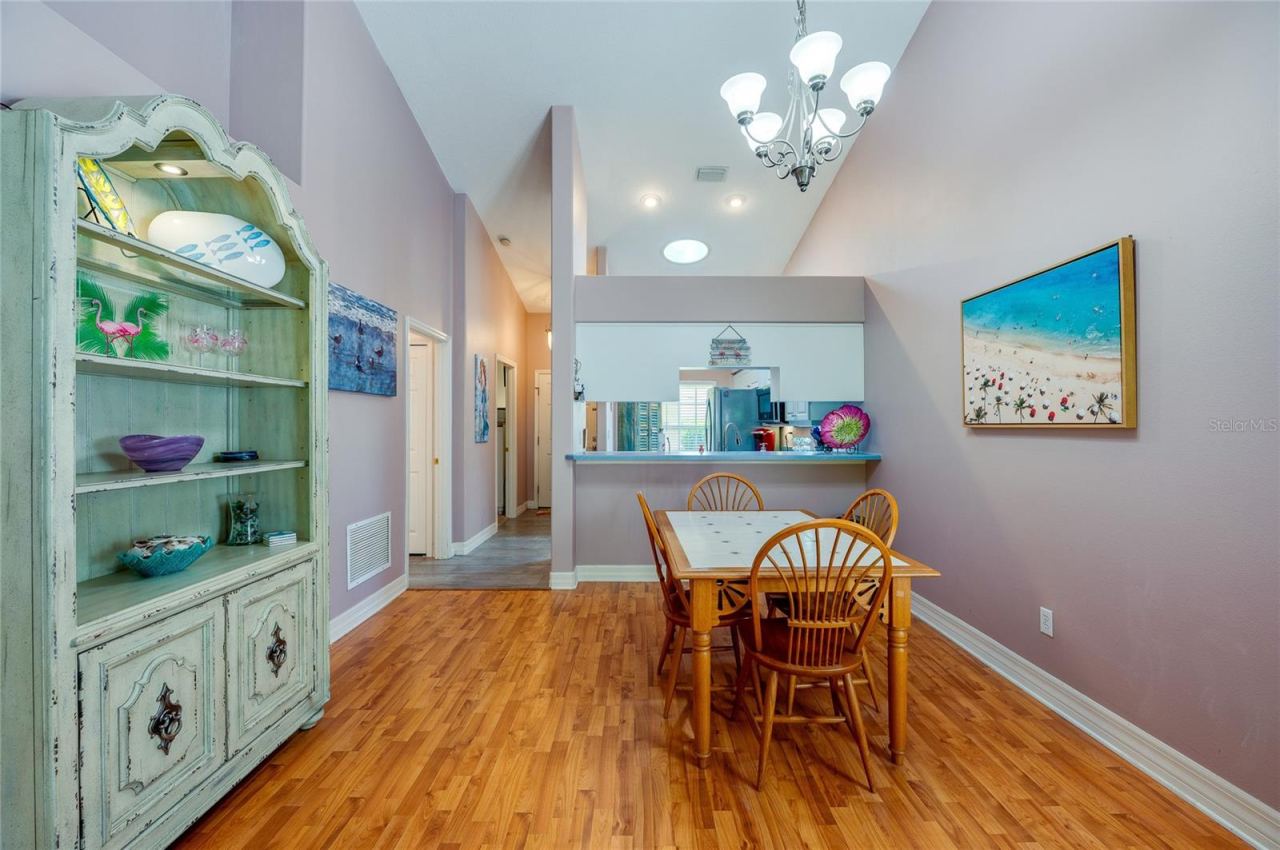 Photo 7 of 20: Open dining space featuring rich laminate flooring, high vaulted ceilings, and a central chandelier. A cutout wall provides a direct view into the kitchen, enhancing the overall flow.
