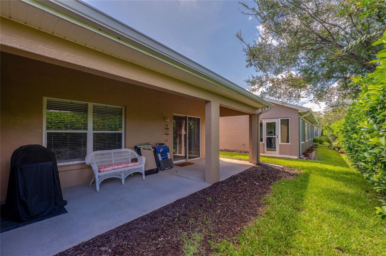 Photo 18 of 20: Sheltered back patio with concrete flooring leading out to a lush lawn area. Large glass sliding doors and windows provide easy indoor-outdoor flow along the exterior.
