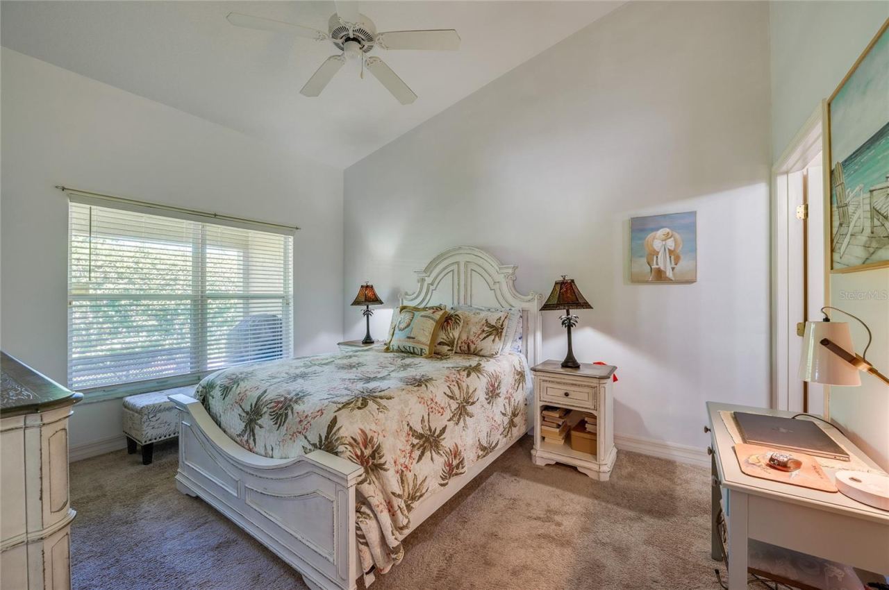 Photo 11 of 20: Serene bedroom suite featuring vaulted ceilings, soft neutral wall tones, and plush carpeting. A large window with horizontal blinds fills the room with indirect light.