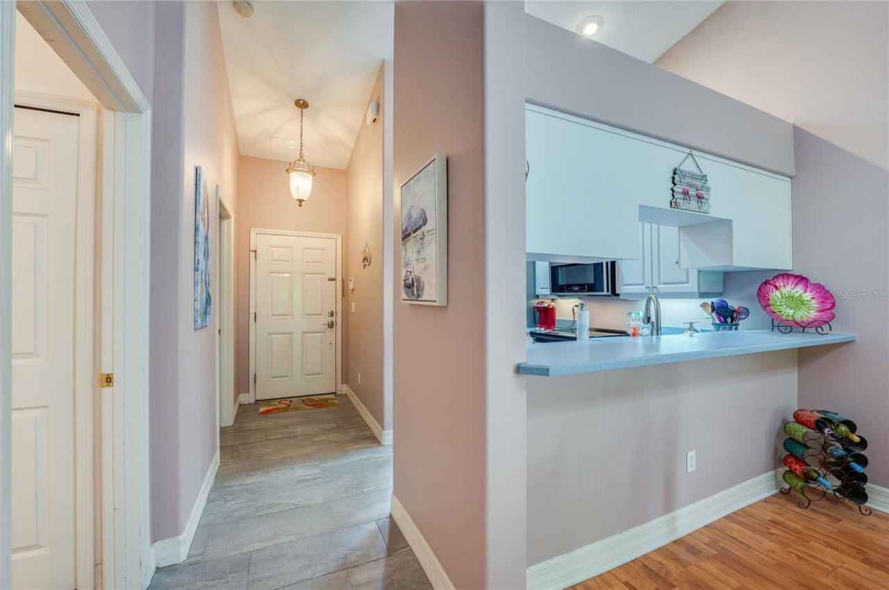 Photo 4 of 20: Welcoming home entrance featuring light grey tile flooring, soft purple walls, and a hanging light fixture. A raised breakfast bar overlooks the foyer, creating an open-concept flow.