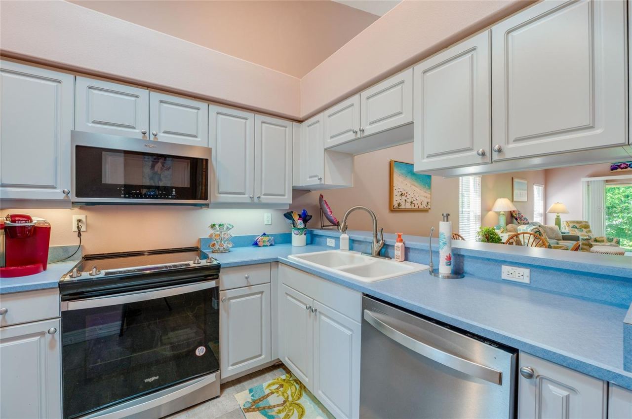 Photo 6 of 20: Efficient kitchen layout highlighting a built-in dishwasher, electric range, microwave, and double-basin sink. A pass-through window maintains a seamless connection to the adjacent living area.