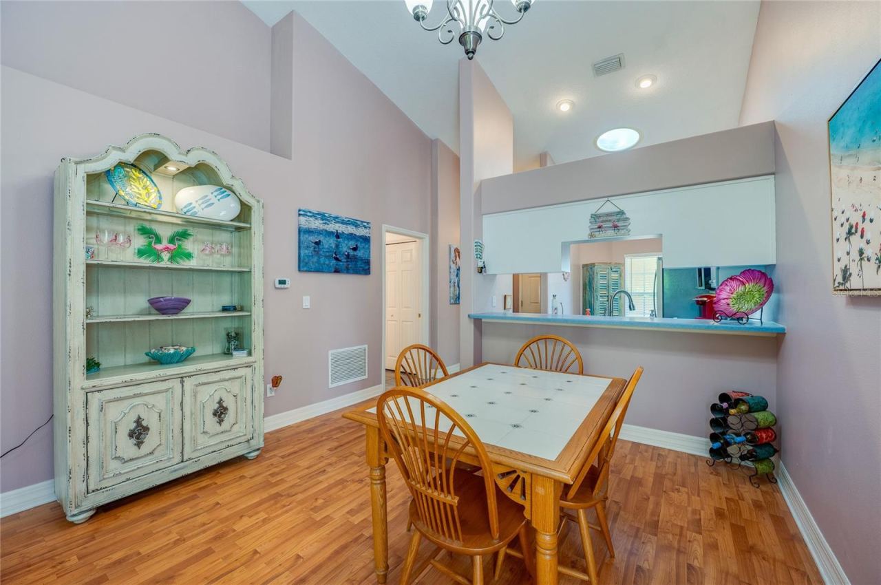 Photo 8 of 20: Light-filled dining space featuring high vaulted ceilings, modern overhead lighting, and rich laminate flooring. A low partition wall with a pass-through counter offers a seamless connection directly into the kitchen.