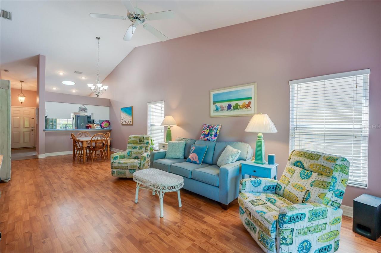 Photo 10 of 20: Expansive open-concept main living area defined by high ceilings and continuous laminate flooring. Large windows flood the space with natural light, connecting the front entry, kitchen pass-through, and living space.