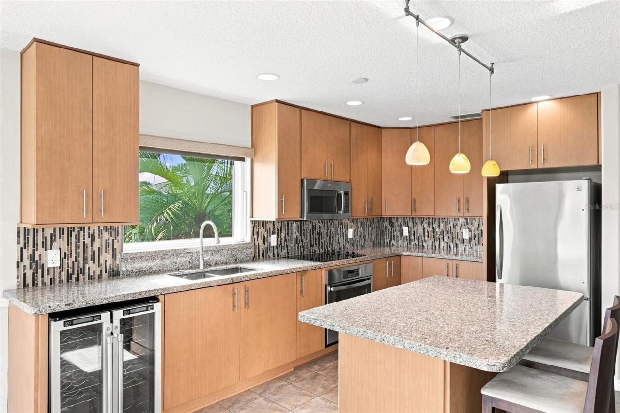 Photo 19 of 20: Kitchen entry — Kitchen opening to a French door leading to a screened porch, with chandelier, granite island, and staircase visible in the background.