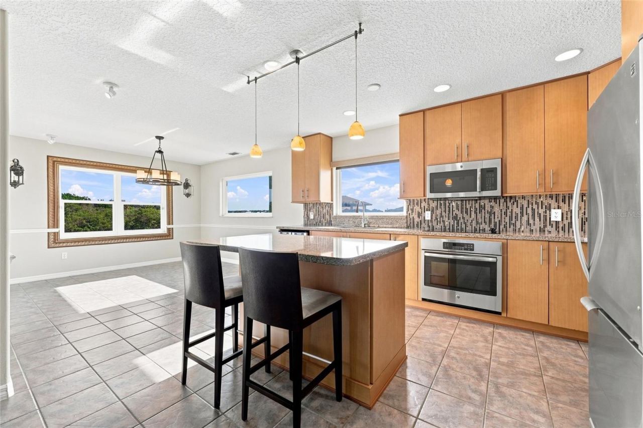 Photo 13 of 20: Kitchen — Renovated kitchen with granite island seating two, pendant lighting, glass tile backsplash, and stainless steel appliances with a canal view through the window.