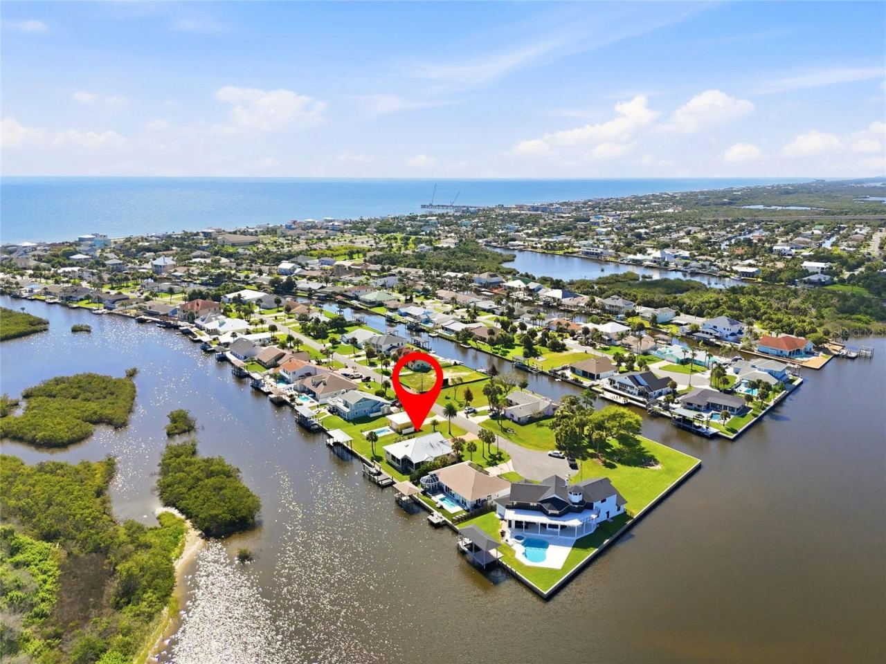 Photo 1 of 20: Aerial view — Aerial view of the canal-front property showing direct water access to the Intracoastal Waterway, with two covered boat lift areas on the dock, a backyard pool, detached garage, and mature palm landscaping