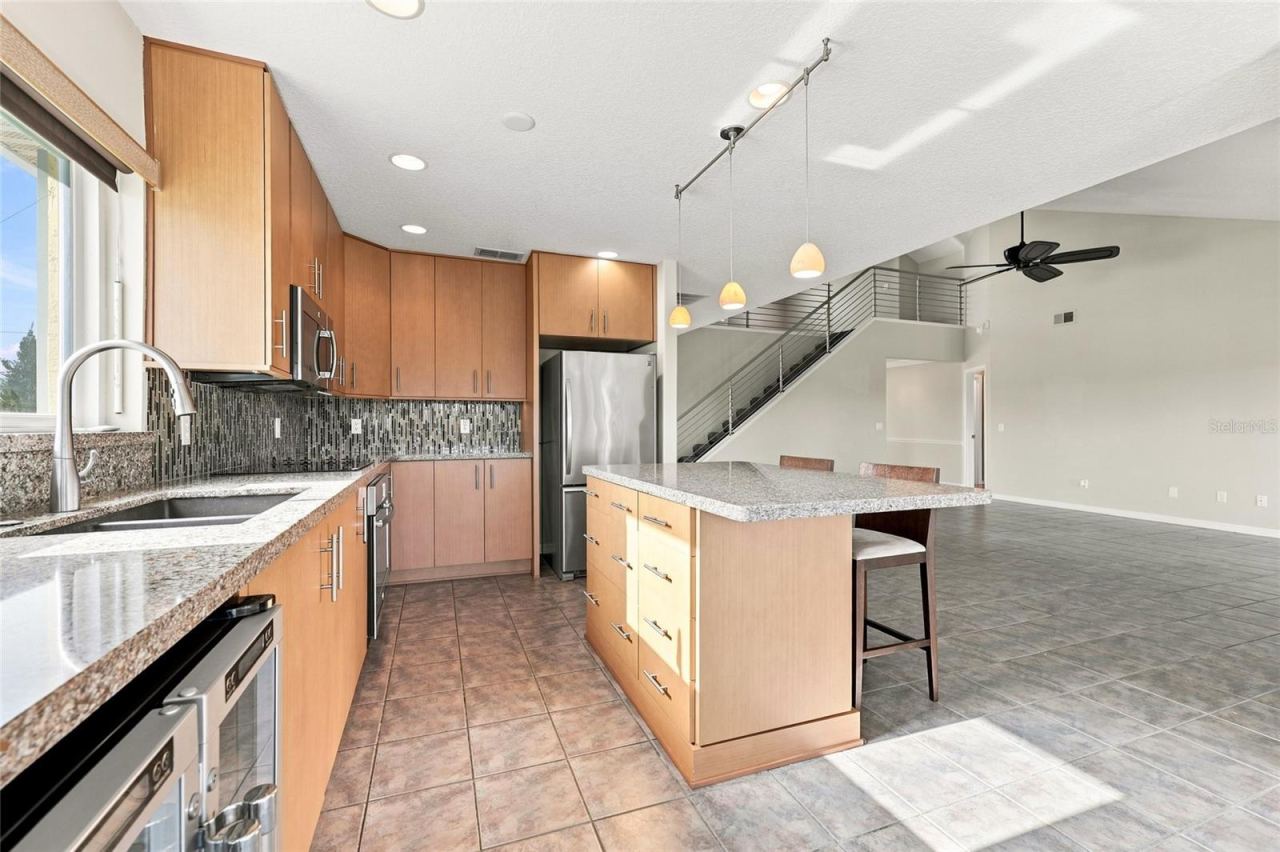 Photo 16 of 20: Kitchen — Kitchen view toward the staircase and open living area, with granite island, stainless refrigerator, and pendant lighting.