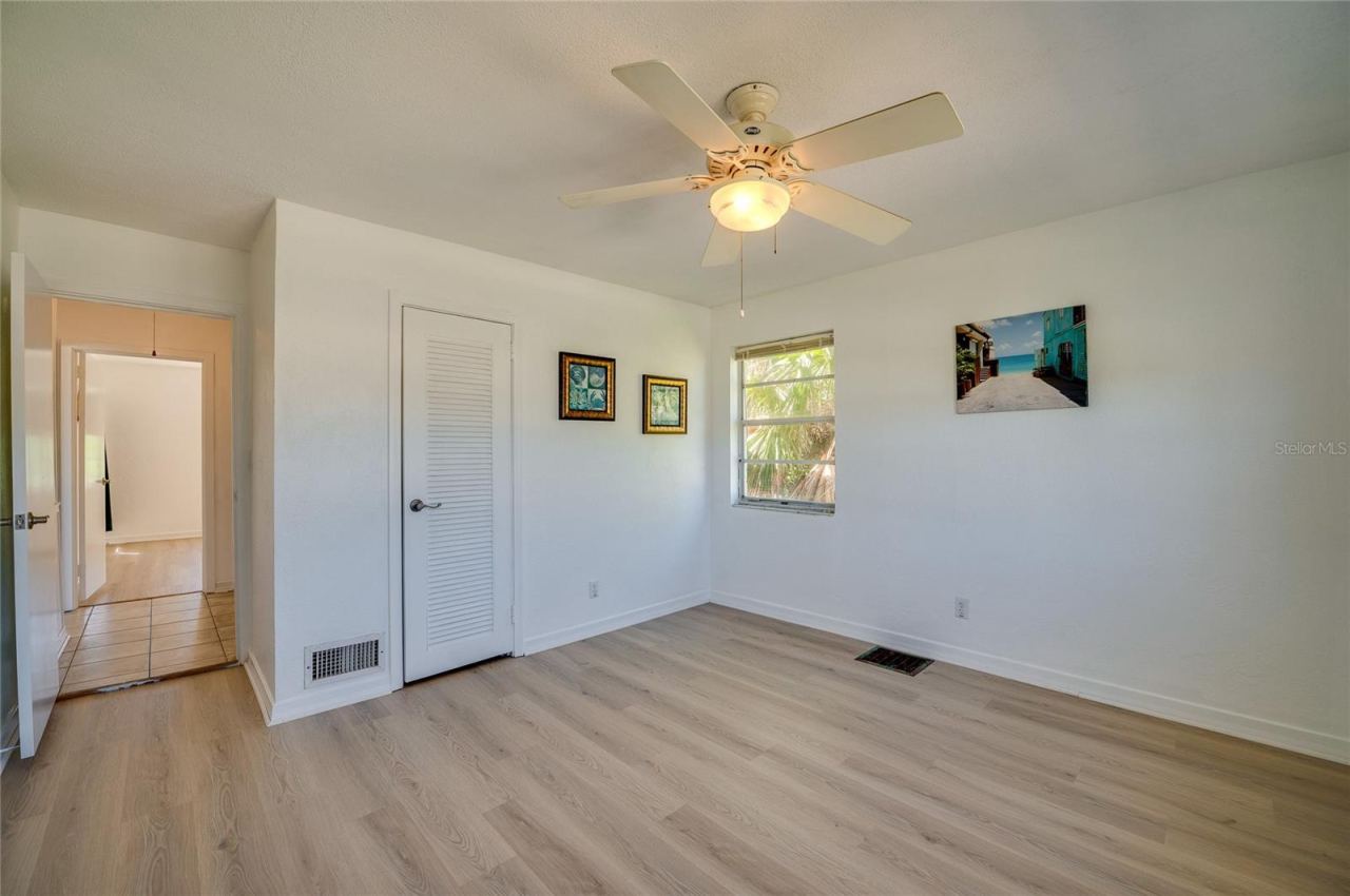 Photo 19 of 20: Clean interior space showcasing light flooring, a white ceiling fan, and a louvered closet door. An open doorway leads out into a tiled hallway connecting to the rest of the layout.