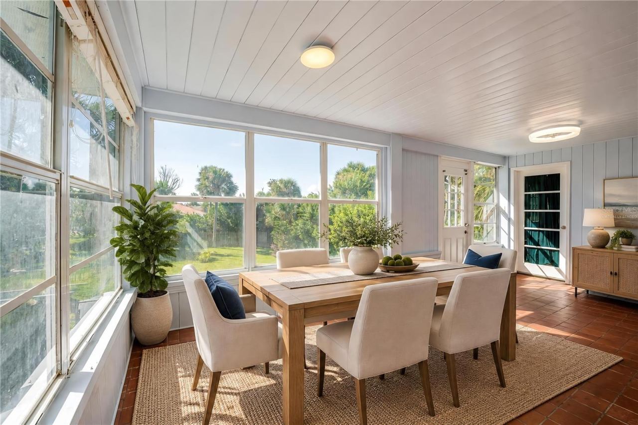 Photo 13 of 20: Virtually Staged - Breakfast nook featuring red tile floors, light-colored wood paneling, flush-mount ceiling lights, and wide windows overlooking the green backyard. Exterior glass doors provide easy access to the lawn and surrounding grounds.