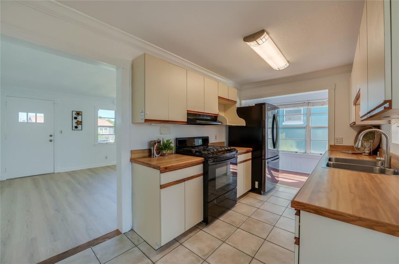 Photo 9 of 20: Efficient kitchen layout showcasing overhead cabinet storage, a gas range stove with range hood, and tile flooring. The open entryway offers a clear view into the adjoining bright living space.