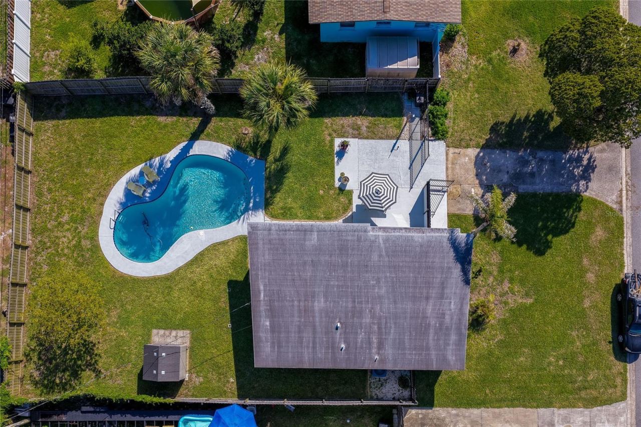 Photo 4 of 20: Direct top-down aerial view detailing the property's layout, including the home’s roof, a paved patio with a seating area, an immaculate lawn, and a swimming pool.
