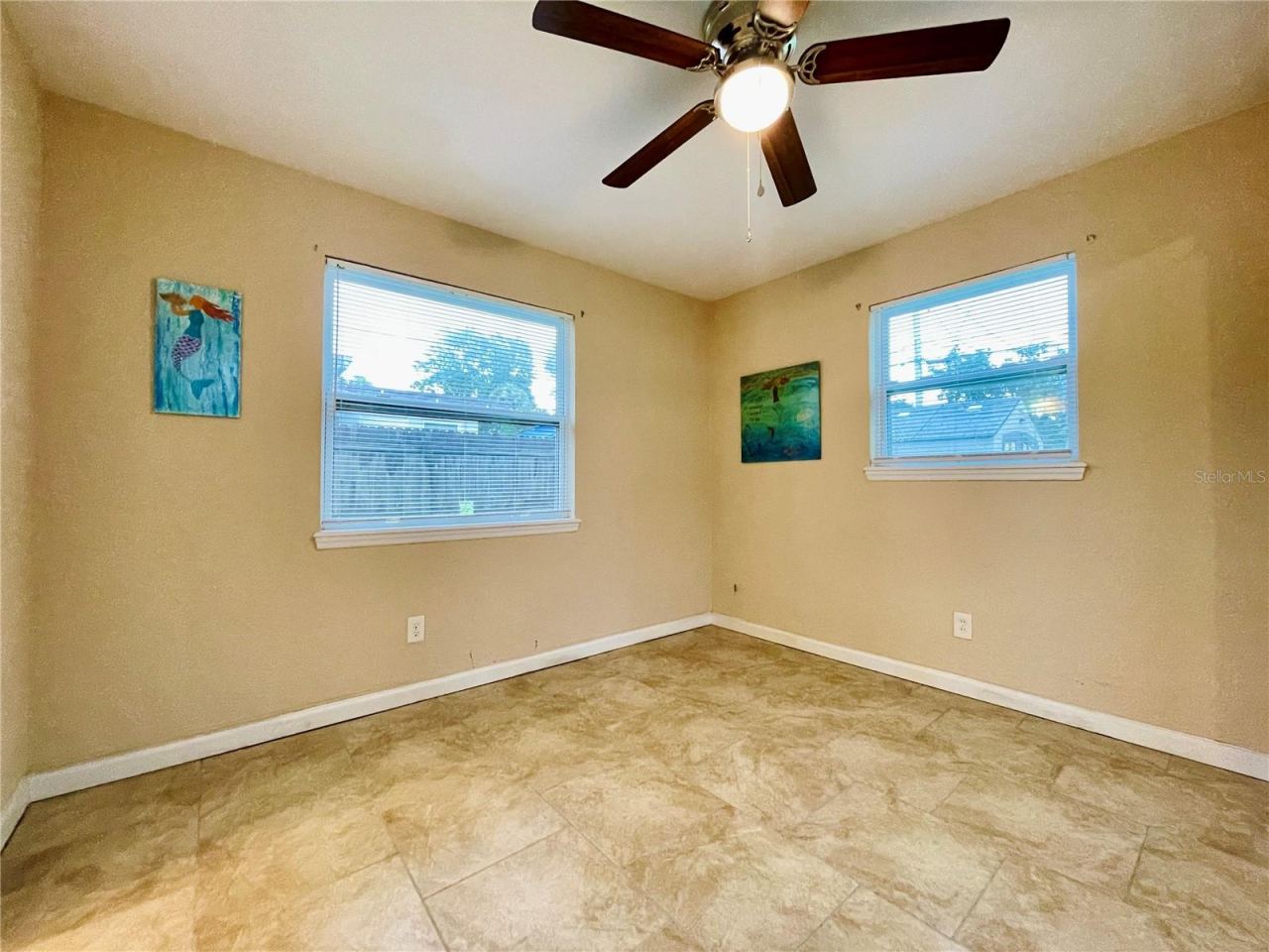 Photo 14 of 20: Cozy bedroom featuring warm tan walls, tile flooring, and ample natural light from two windows.