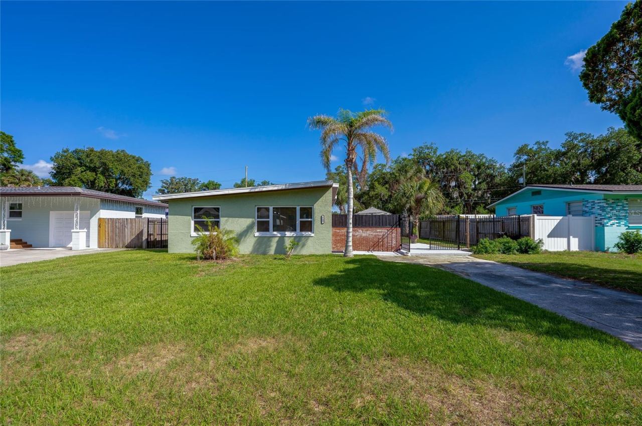 Photo 3 of 20: Front exterior of a charming, light green mid-century modern home showcasing a distinctive sloped roofline, a manicured lawn, and a palm tree.