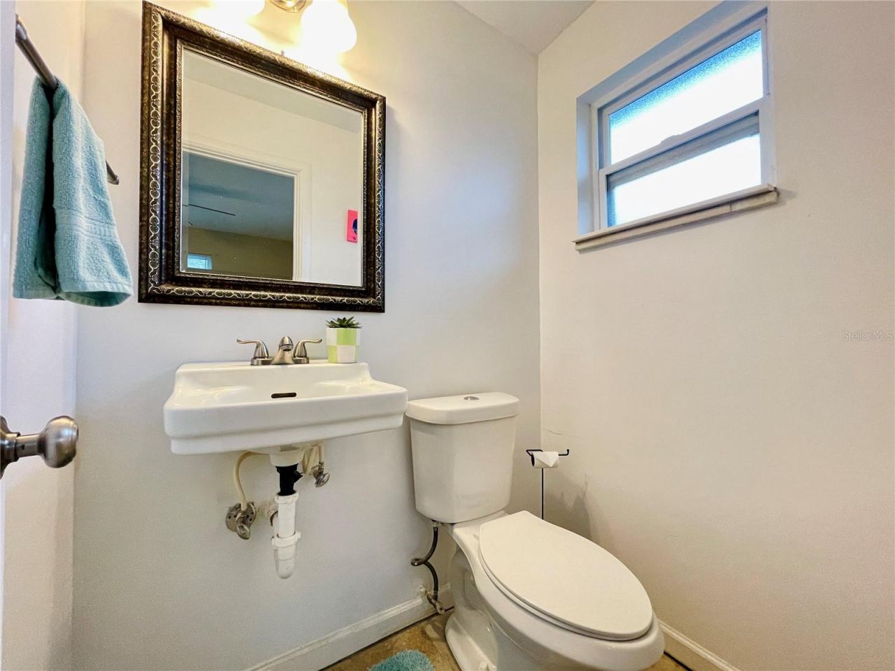 Photo 16 of 20: Functional half-bathroom off the bedroom with equipped with a classic wall-mounted sink, a decorative framed mirror, and a frosted privacy window.