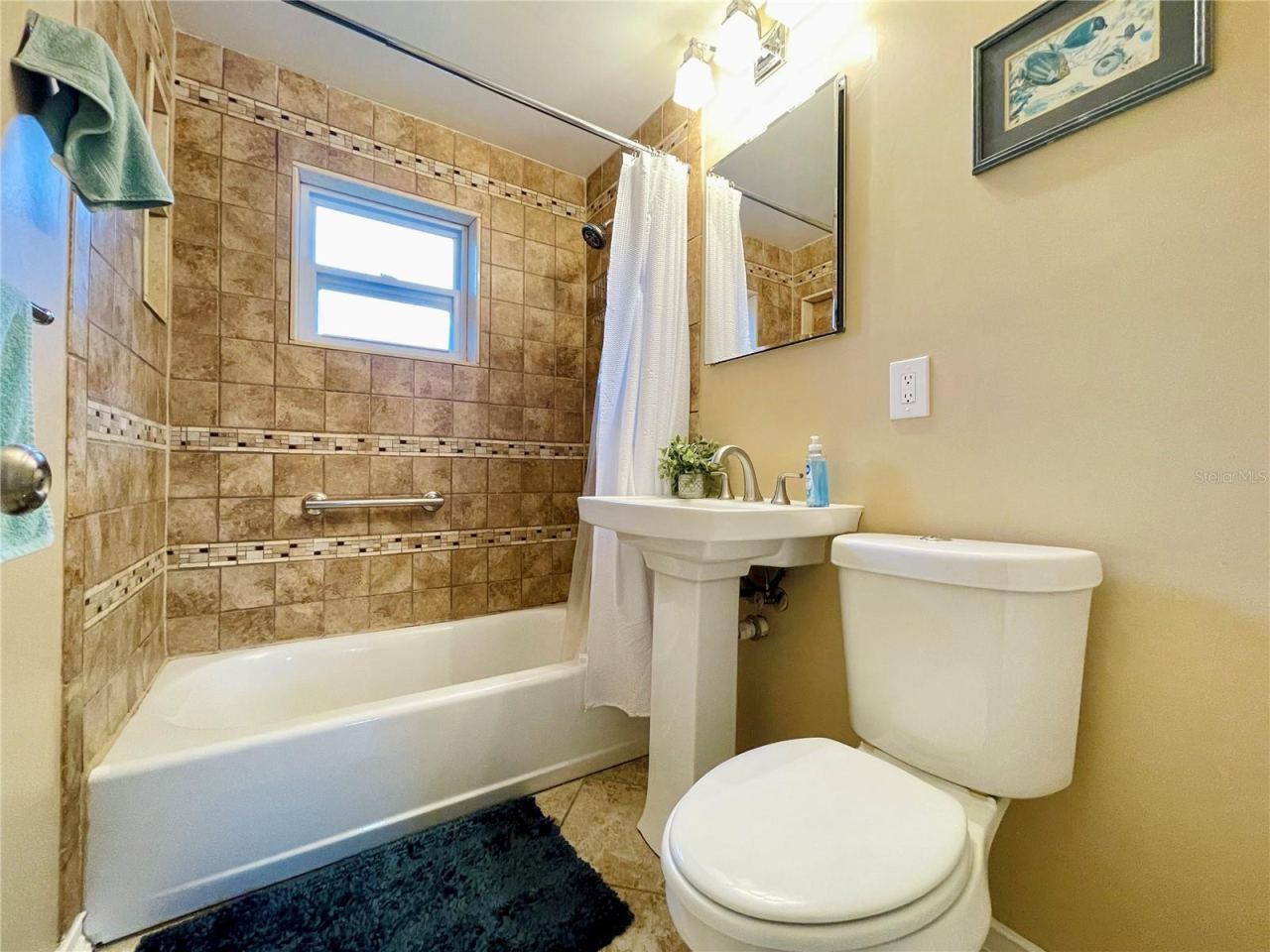 Photo 19 of 20: Full bathroom accented by floor-to-ceiling wall tiles, a classic pedestal sink, and a combination bathtub and shower.