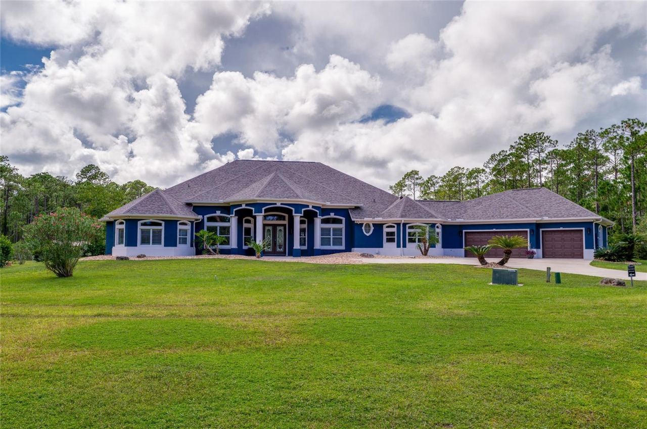Photo 2 of 20: Front exterior shot of the blue home showing distinct architectural rooflines, columns, and a multi-car garage.