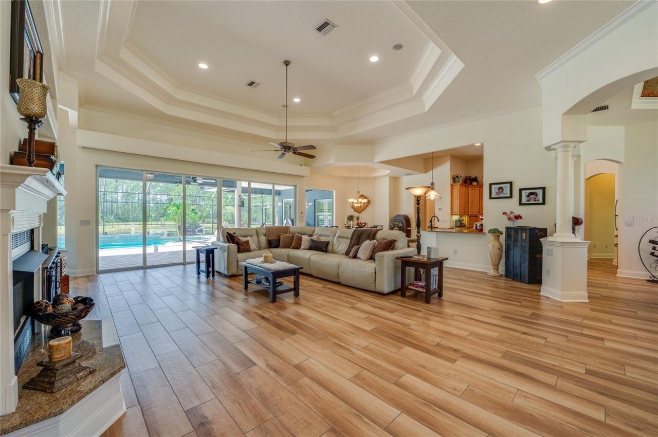 Photo 19 of 20: Spacious open floor plan showcasing high multi-tier tray ceilings, a built-in fireplace, and large sliding glass doors opening up to the screened pool patio.