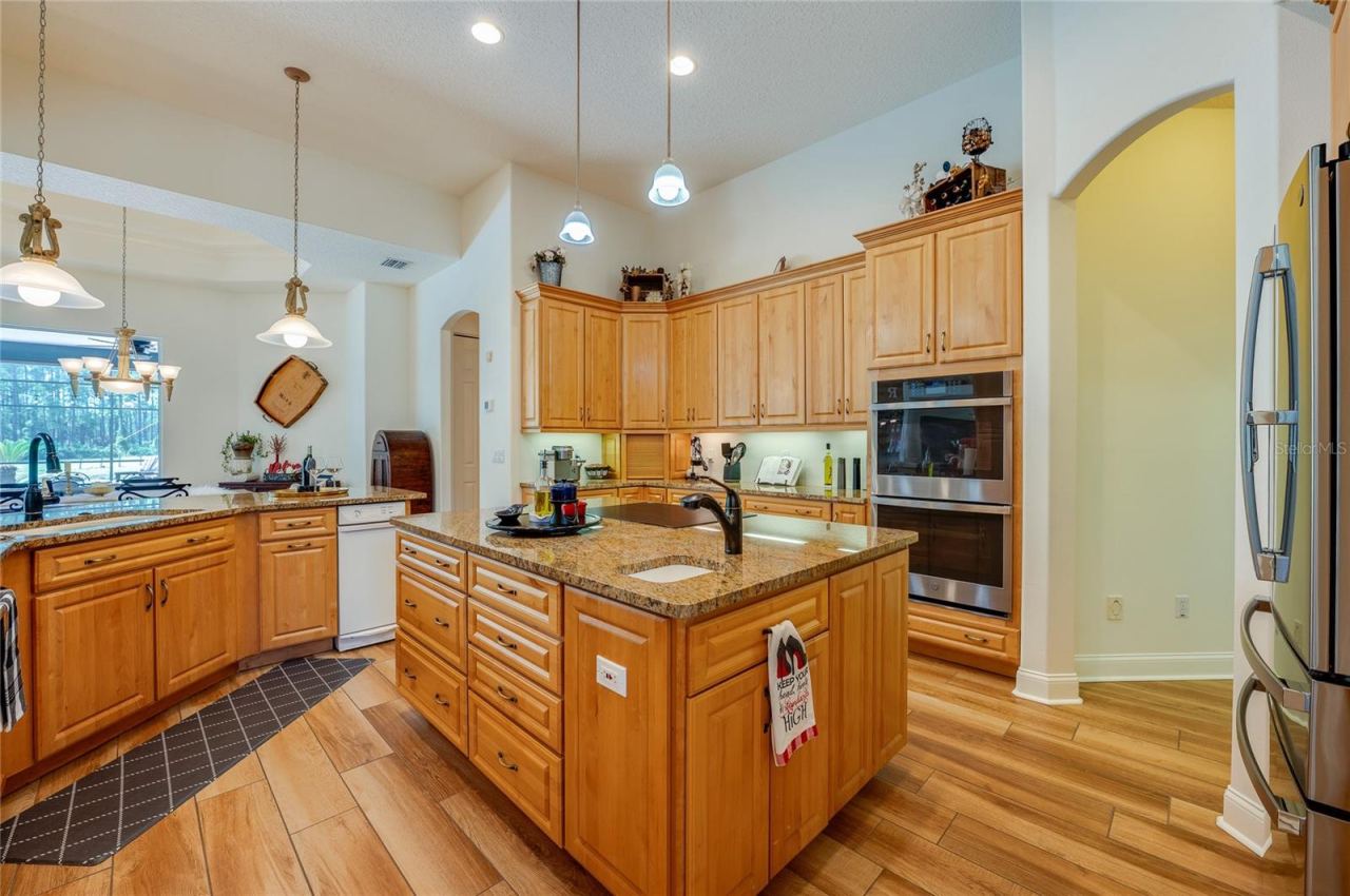 Photo 15 of 20: Functional open kitchen layout complete with double wall ovens, rich wood cabinetry, a prep island with sink, and recessed lighting.