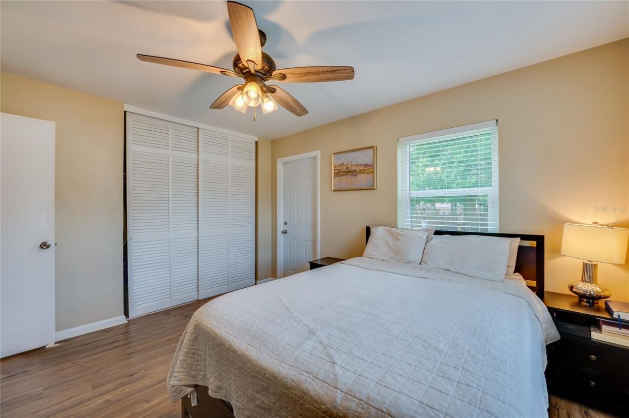 Photo 15 of 20: Spacious bedroom featuring warm LVP flooring, white louvered sliding closet doors, and multiple windows allowing plenty of natural light.