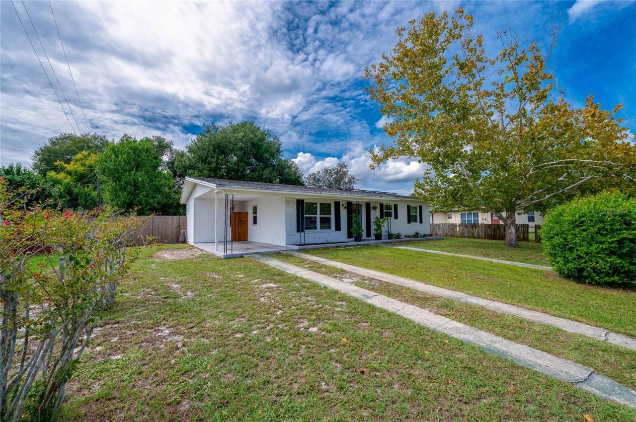 Photo 2 of 20: Exterior view highlighting the long concrete ribbon driveway, expansive front lawn, mature shade trees, and low-maintenance single-story design.