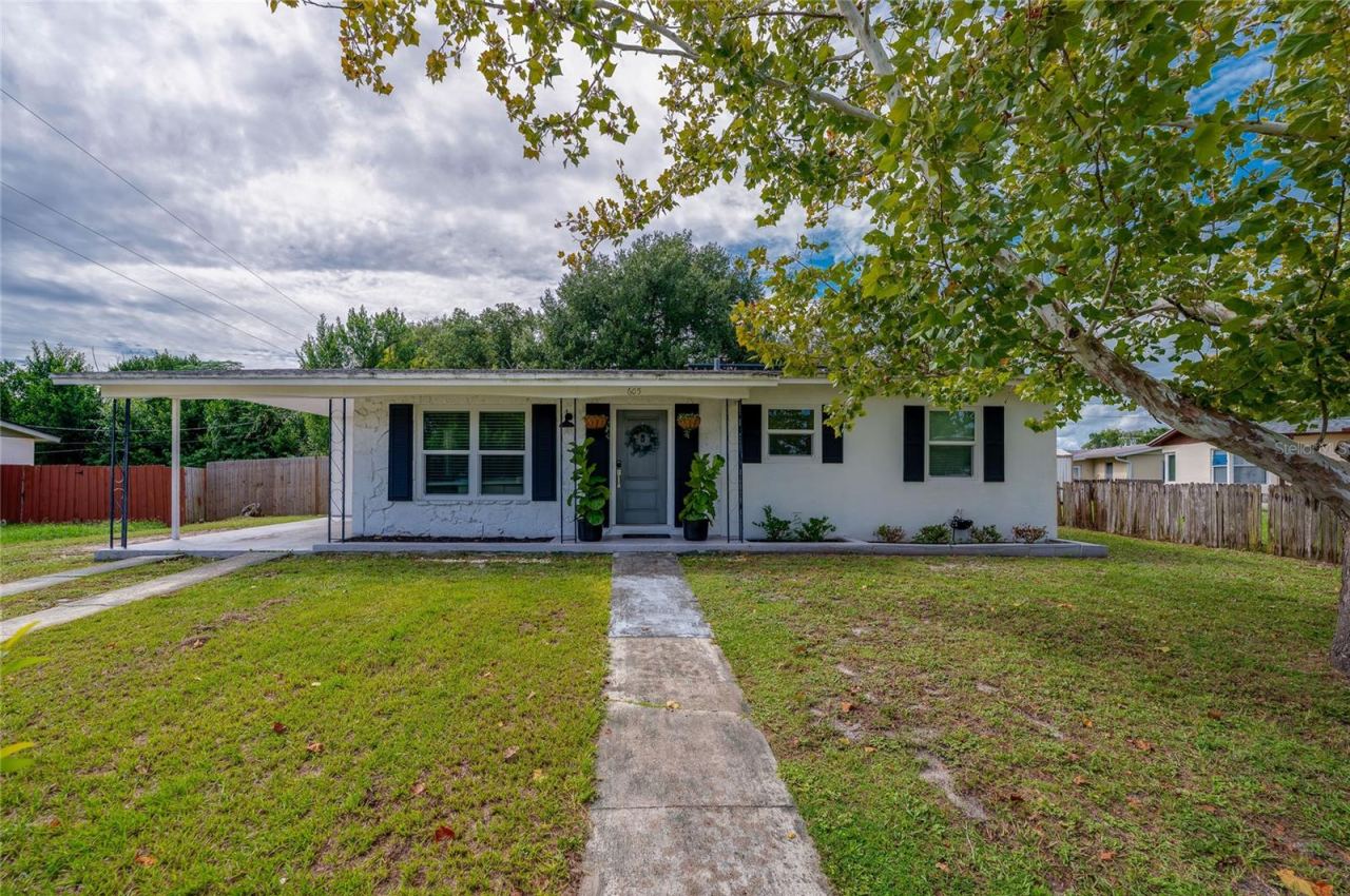 Photo 1 of 20: Charming single-story home exterior featuring crisp white siding, dark accent shutters, a covered carport, and a paved walkway crossing a spacious front lawn.