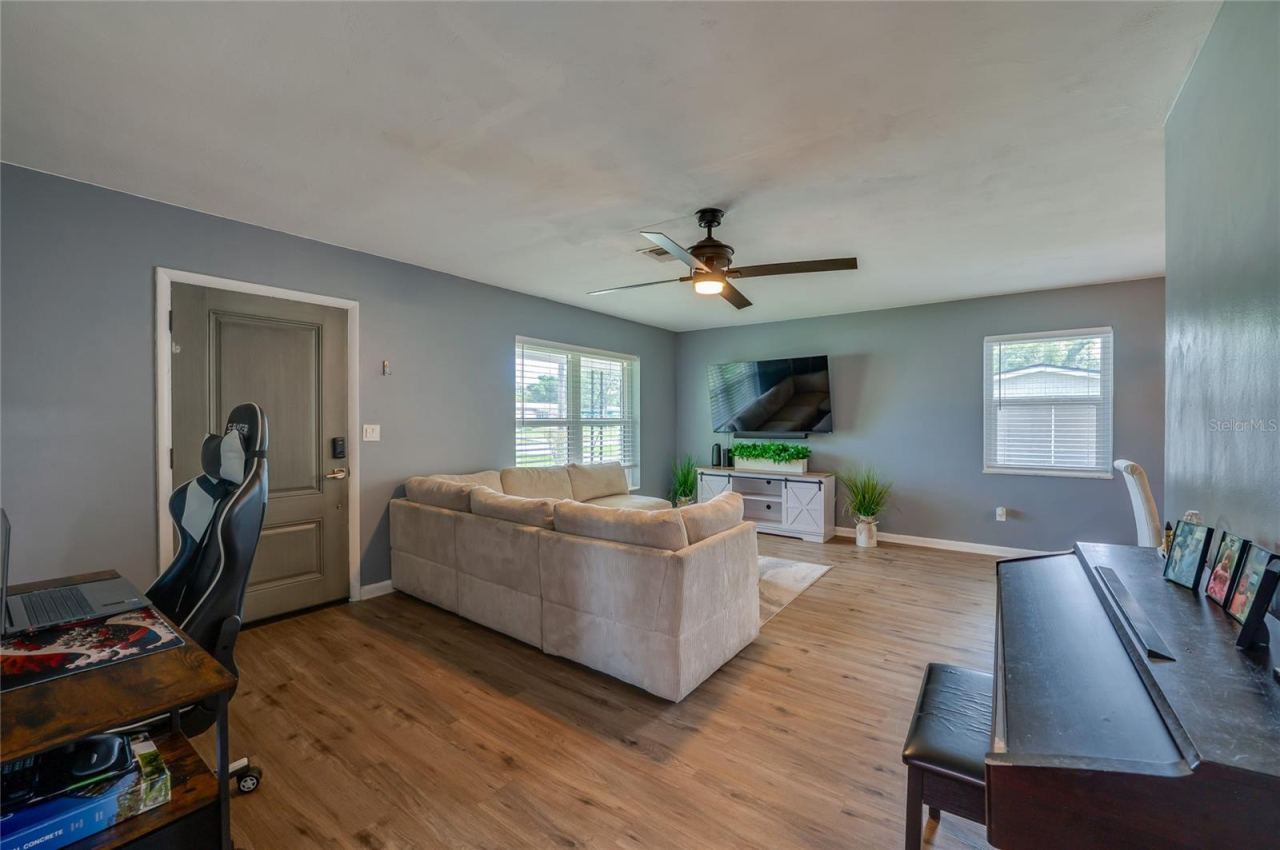 Photo 5 of 20: Open living area showing LVP floors, cool gray walls, a ceiling fan, and large windows that fill the space with light.