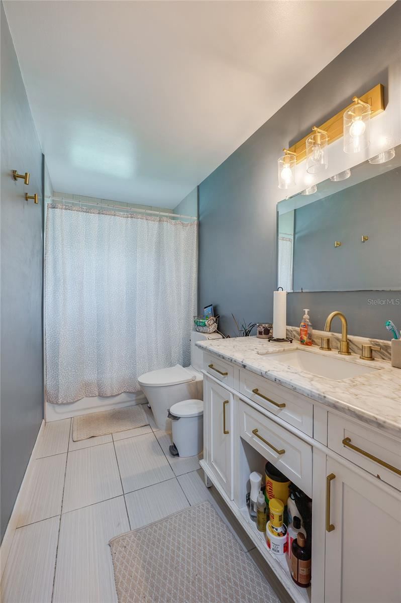 Photo 18 of 20: Bathroom displaying a single vanity with gold hardware, modern lighting fixtures, neutral tile flooring, and clean wall finishes.
