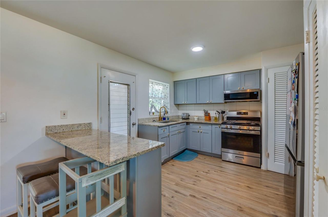 Photo 11 of 20: Functional kitchen layout displaying blue cabinetry, granite counter space, stainless steel appliances, and built-in breakfast bar overhangs.