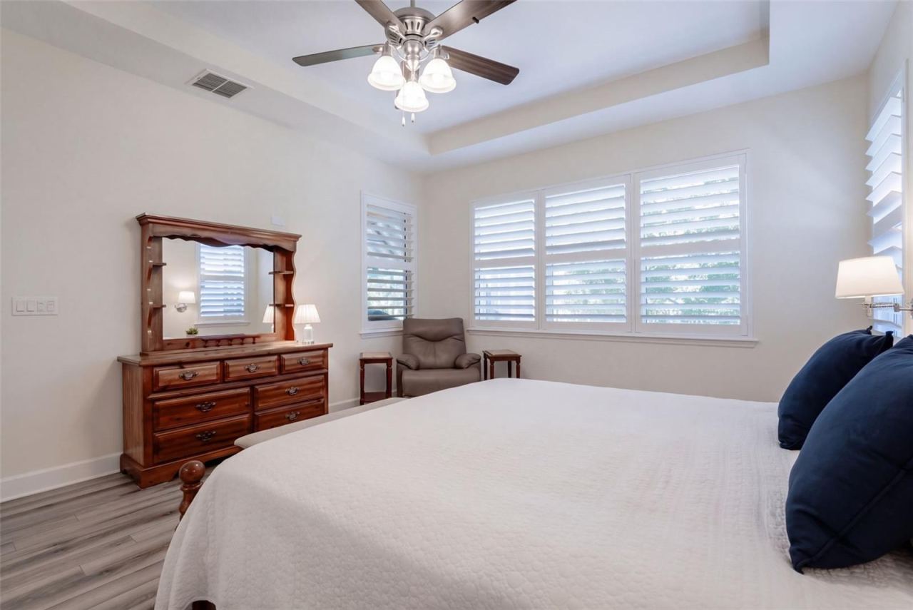 Photo 16 of 20: Primary Bedroom w/ Plantation style shutters, luxury vinyl floor, ceiling fan & a wooded view