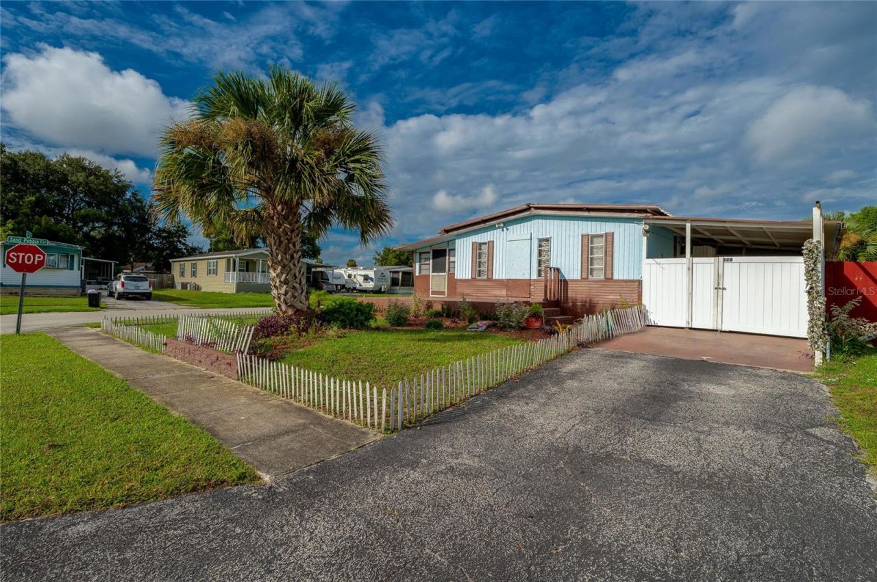 Photo 2 of 20: Front view showcases the home’s landscaped yard, mature palm tree, driveway, covered parking area, and welcoming entry.
