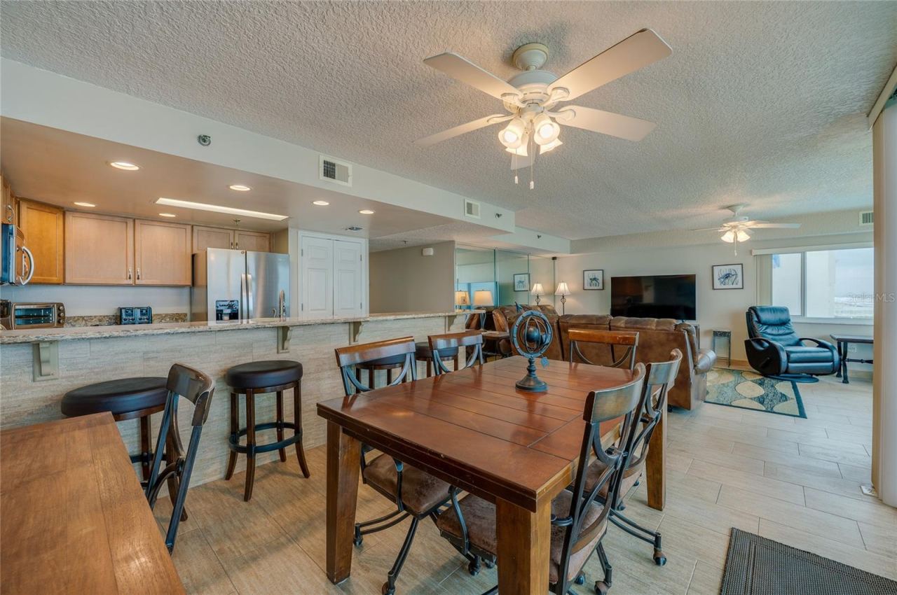 Photo 15 of 20: A central dining area connects to the kitchen and living space, all under ceiling fans and surrounded by windows—ideal for casual meals and gatherings.