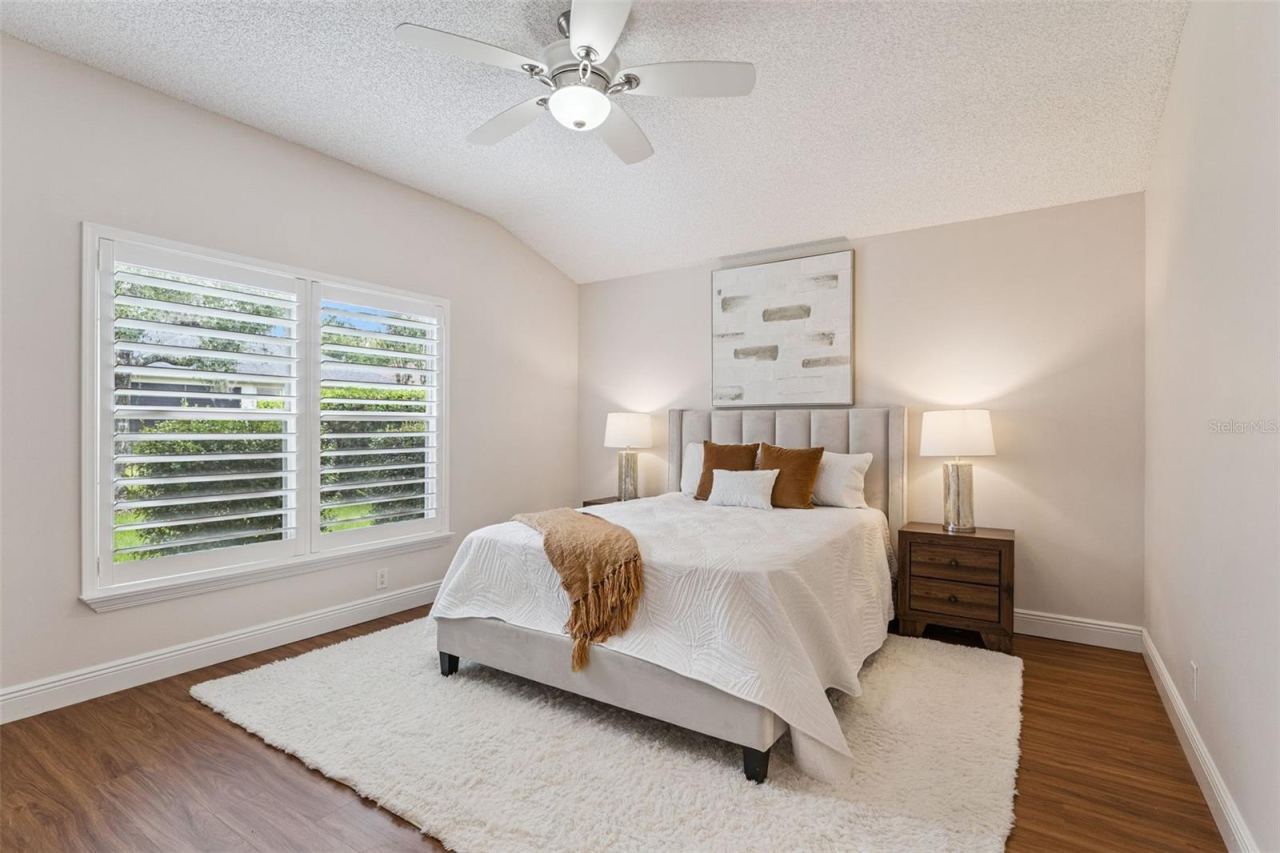 Photo 17 of 20: 15'6" x 12'6" Primary Bedroom w/ a laminate floor, ceiling fan & Plantation style shutters