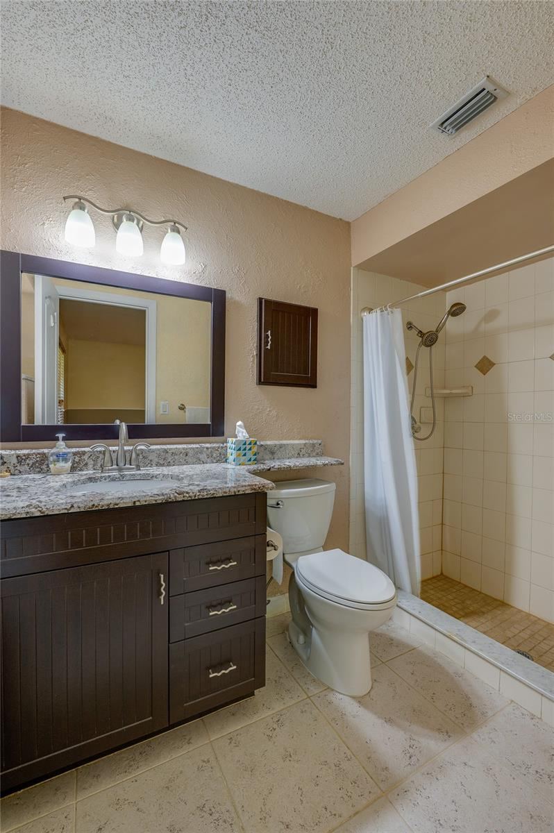 Photo 20 of 20: Primary bathroom showcasing a dark wood vanity with granite countertops, tiled flooring, a wide framed mirror, and a walk-in tiled shower.