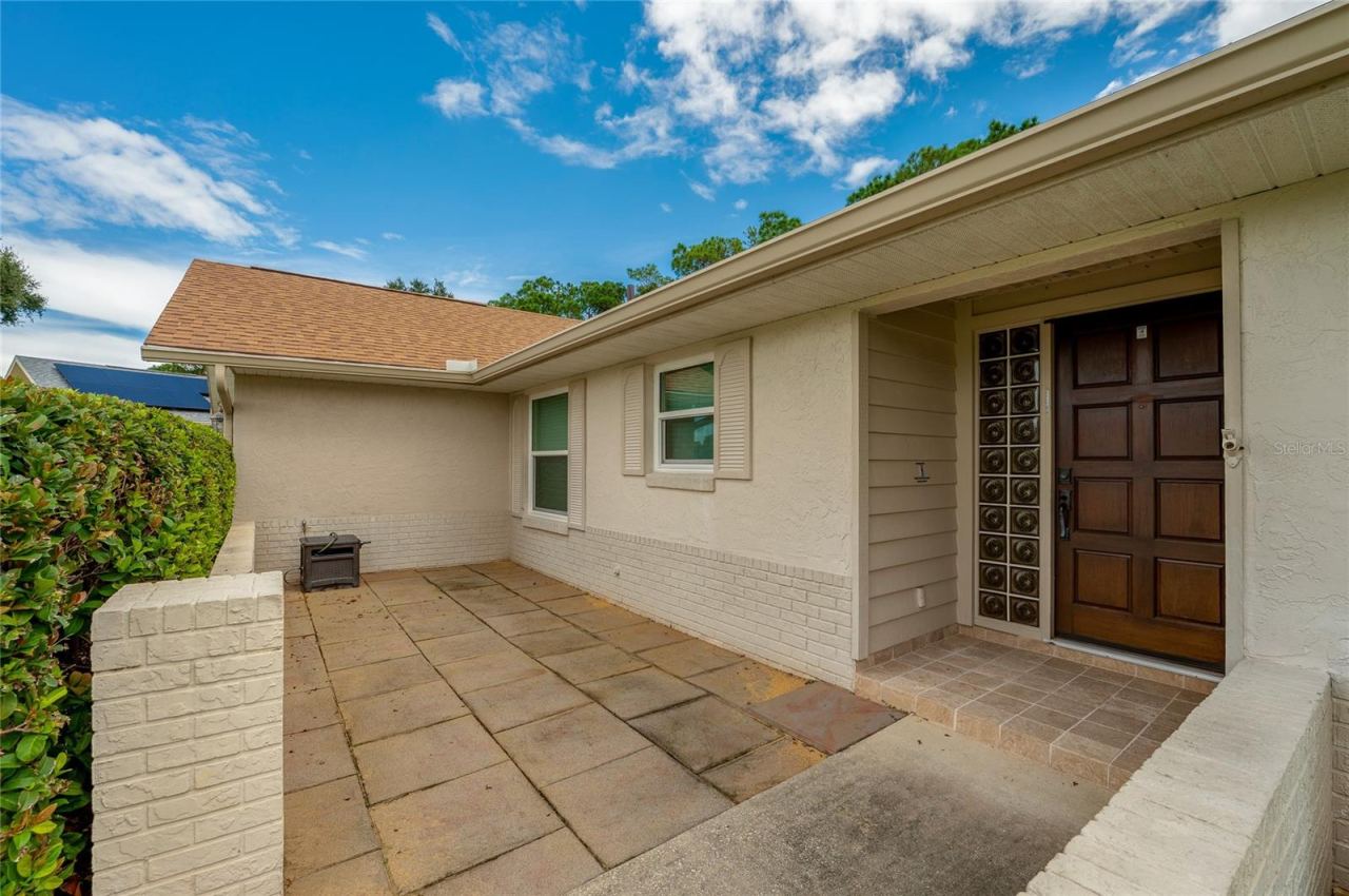 Photo 5 of 20: Welcoming front entry patio framed by brick half-walls, tiled walkways, and decorative glass block accents by the door.